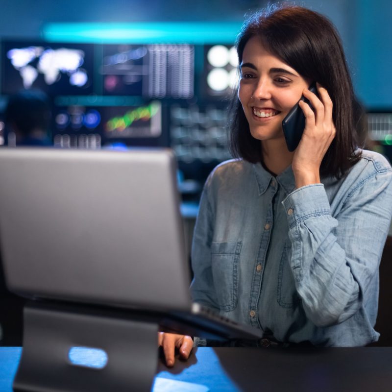 Female stock market trader working in office using laptop and talking on the phone with client. Female stock market trader working in office using laptop and talking on the phone with client. Financial adviser concept.